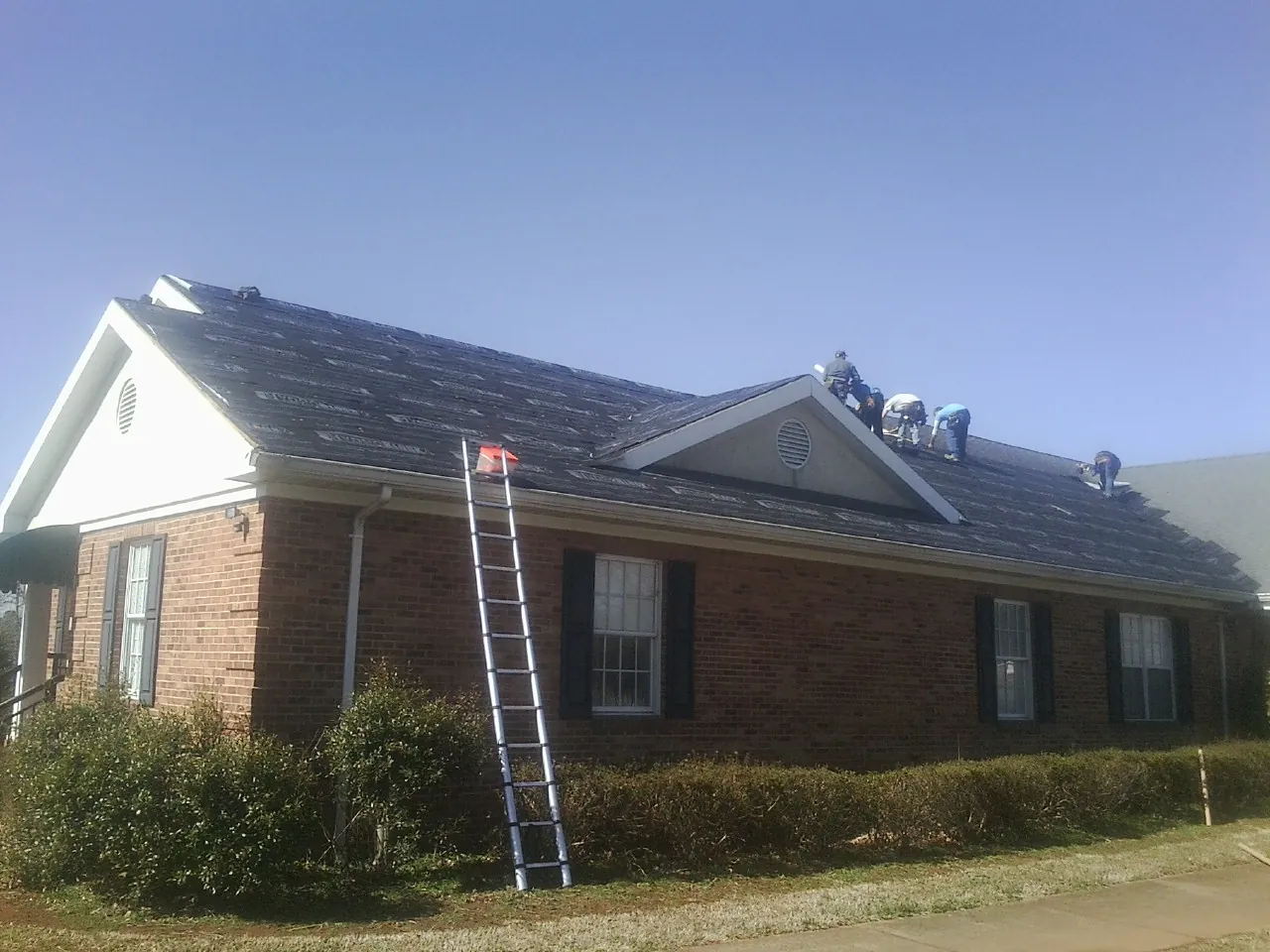 Crew tearing shingles off a brick ranch roof with a ladder set — Emergency Roof Repair work by our crew in Potts Camp