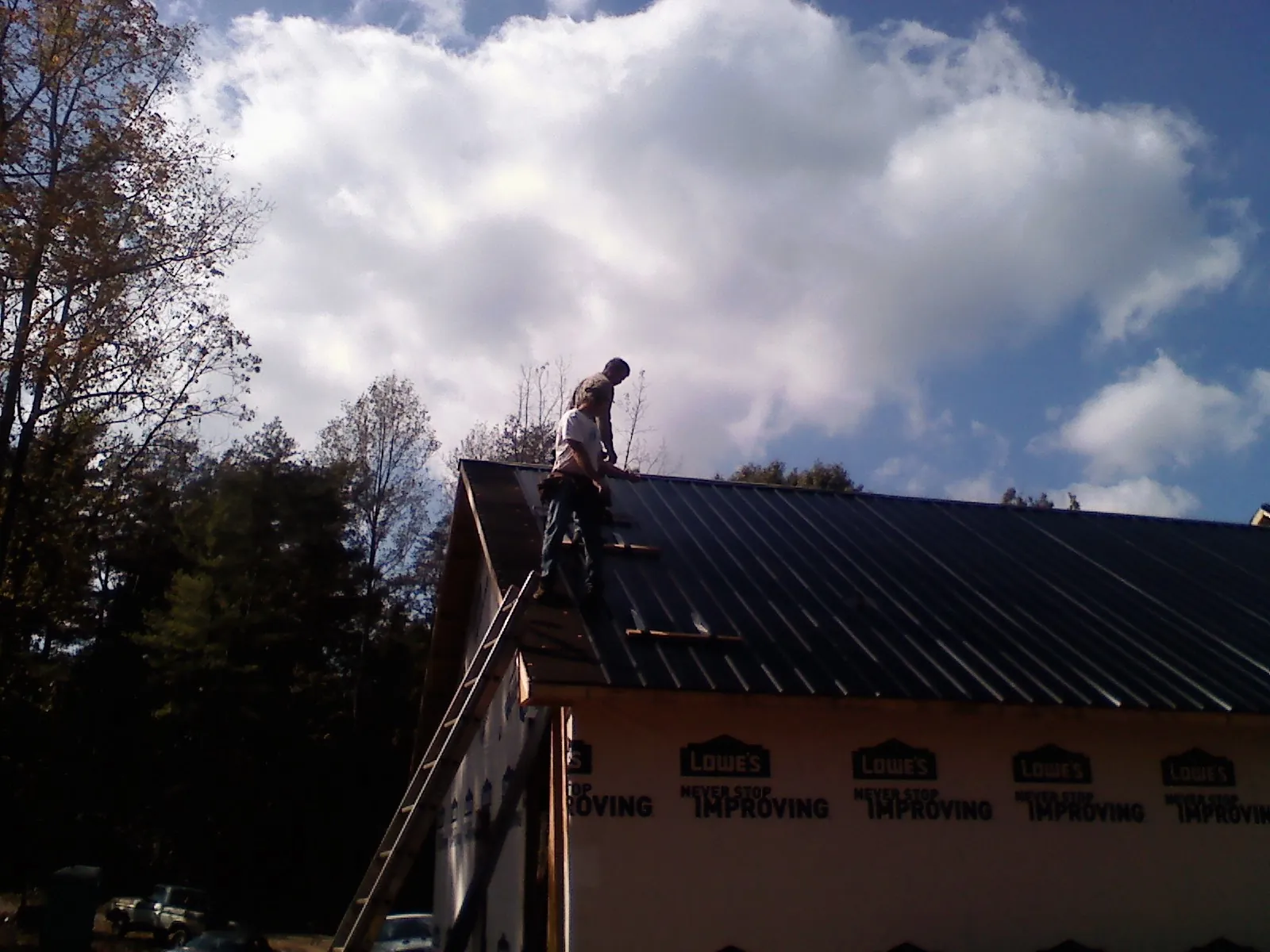 Roofer fastening dark metal panels high against a cloudy sky, from a Roof Inspection job in Potts Camp