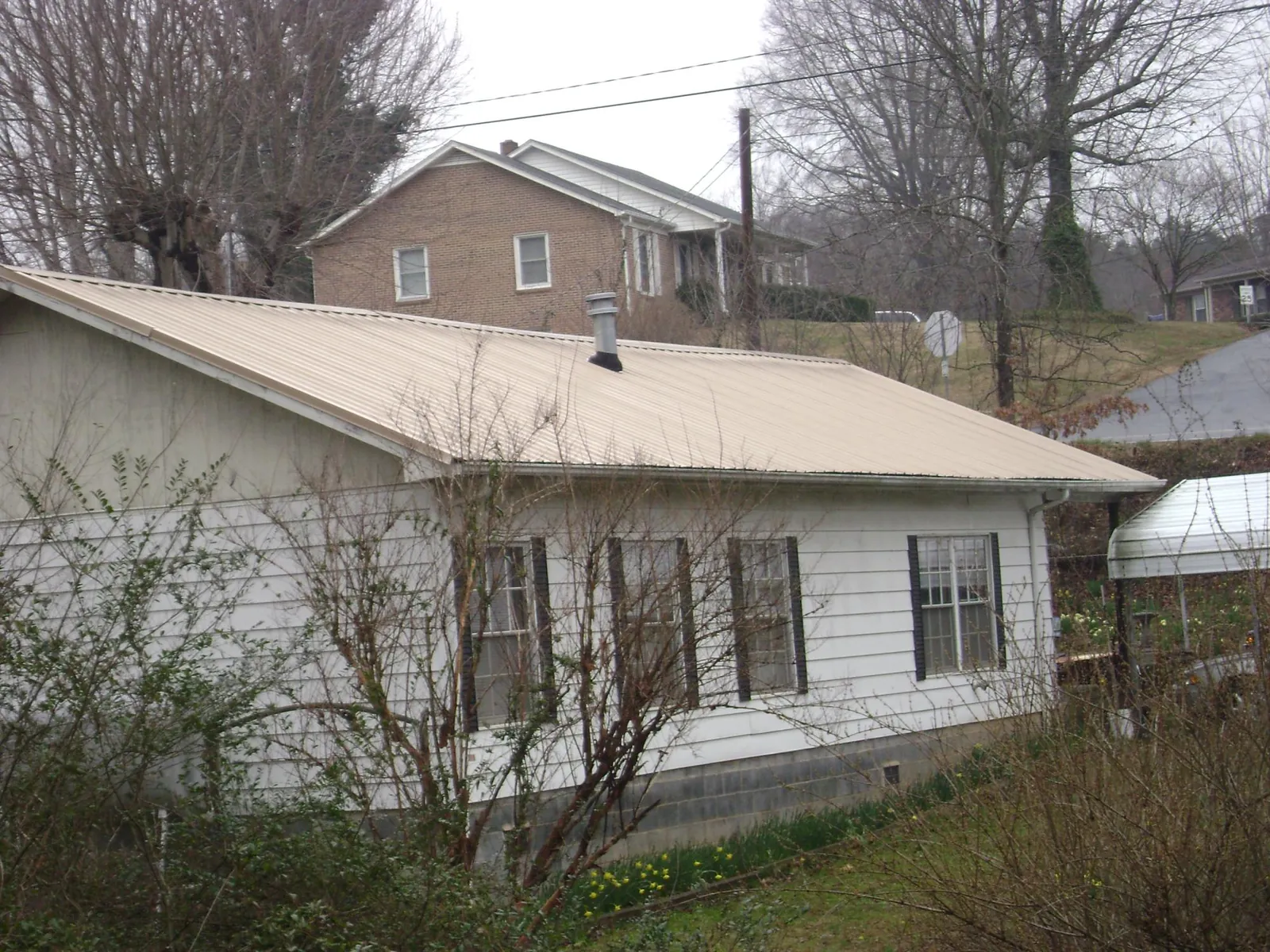Tan metal roof on a white sided house set into a hillside — Commercial Roofing by Roofing Brothers in Potts Camp