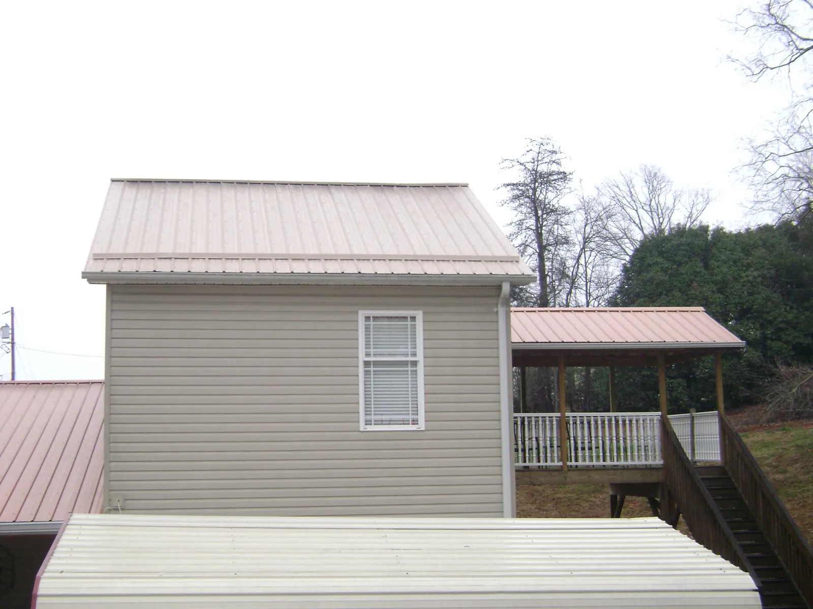 Tan metal roofs on a two story addition and attached porch, from a Roof Replacement job in Potts Camp